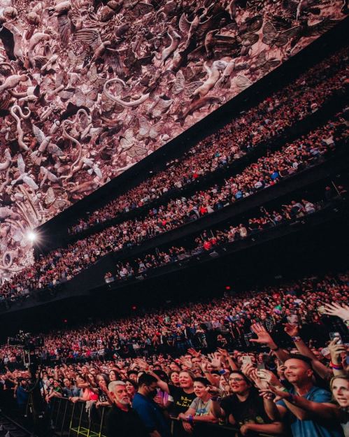 A large crowd at a concert, with a stunning, intricate backdrop above them. Excitement fills the atmosphere.