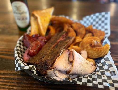 A platter of assorted meats including sliced turkey, sausage, and brisket, served with curly fries and toast.