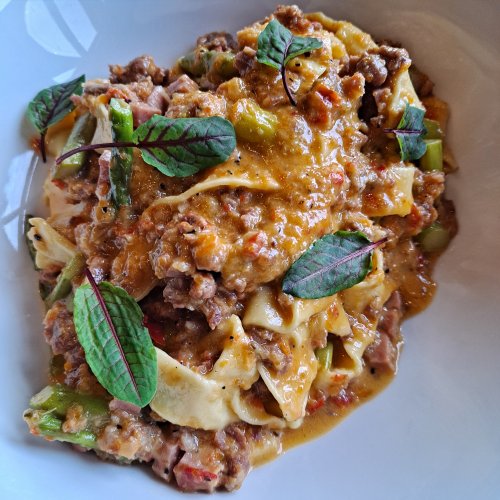 A bowl of pasta with meat sauce, vegetables, and garnished with fresh herbs.