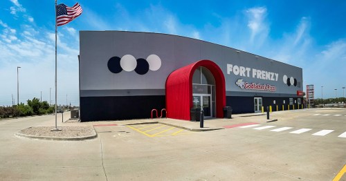 Exterior of Fort Frenzy building with a red entrance, large circular designs, and an American flag in the foreground.