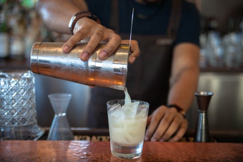 A bartender pours a cocktail from a shaker into a glass filled with ice.