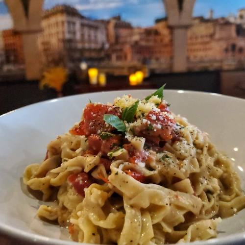 A bowl of pasta topped with tomato sauce, herbs, and cheese, set against a blurred background of a cityscape.