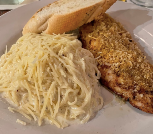 A plate featuring a bread roll, seasoned fish fillet, and a serving of creamy pasta topped with grated cheese.
