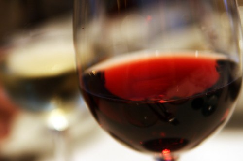 A close-up of a red wine glass in focus, with a blurred white wine glass in the background.