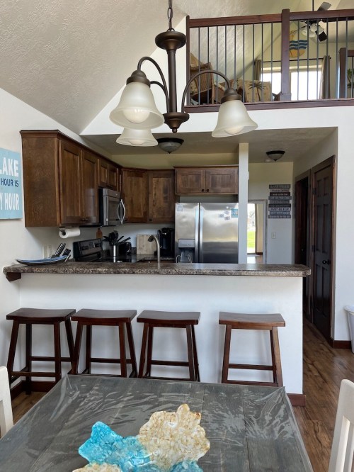Bright kitchen with wooden cabinets, stainless steel appliances, and bar stools, overlooking a cozy dining area.