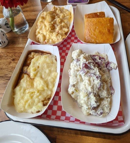 A tray with four dishes: creamy mac and cheese, mashed potatoes, potato salad, and cornbread squares.
