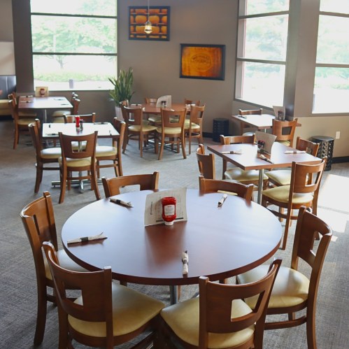 A cozy restaurant interior with wooden tables and chairs, featuring large windows and a simple decor.