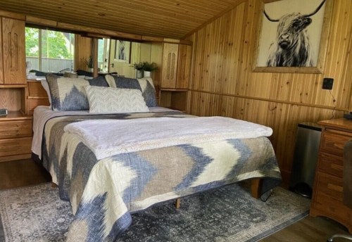 Cozy wooden bedroom with a bed, decorative pillows, and a large wall art of a cow. Warm, inviting atmosphere.