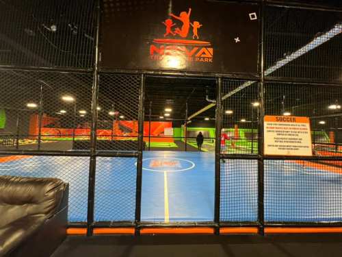 Indoor sports facility with a blue soccer field, surrounded by netting and colorful walls. Signage visible nearby.