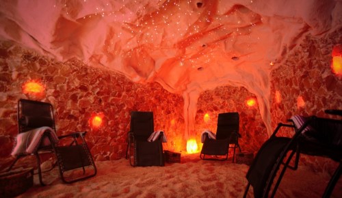 A tranquil salt cave with pink lighting, two reclining chairs, and glowing salt lamps on the walls.