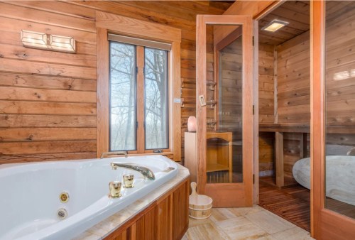 Cozy bathroom featuring a jetted tub, wooden walls, and a glass shower enclosure with natural light.