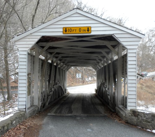 A covered bridge with a height clearance sign, surrounded by trees and a snowy landscape.