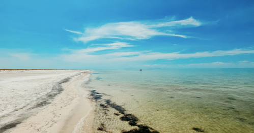 A serene beach scene with clear water, soft sand, and a blue sky with wispy clouds.
