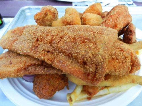 A plate of crispy fried fish fillets, hushpuppies, and golden fries piled high.