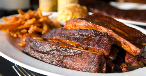 A plate of glazed ribs with sweet potato fries and a side of coleslaw, served in a casual dining setting.