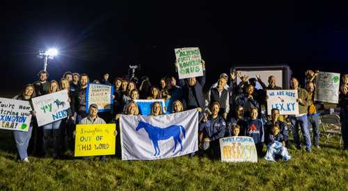 A large group of people holding signs and a flag, celebrating an event at night in a grassy area.