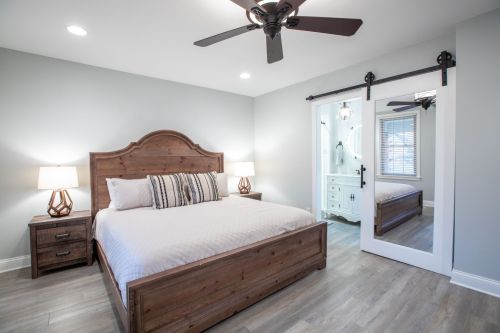Cozy bedroom with a wooden bed, nightstands, ceiling fan, and sliding door leading to a bathroom. Soft lighting.