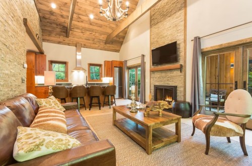 Cozy living room with a leather sofa, wooden coffee table, and a fireplace, featuring rustic decor and warm lighting.