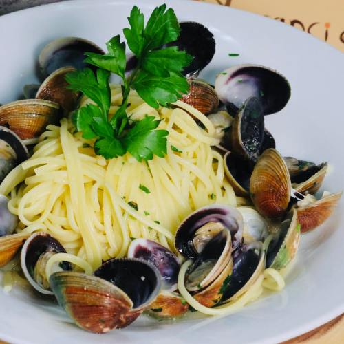 A bowl of spaghetti topped with clams and garnished with a sprig of parsley.