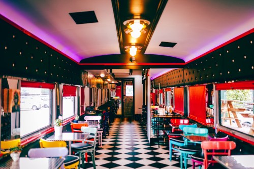 A colorful diner interior with checkered floors, vibrant chairs, and retro lighting, creating a lively atmosphere.