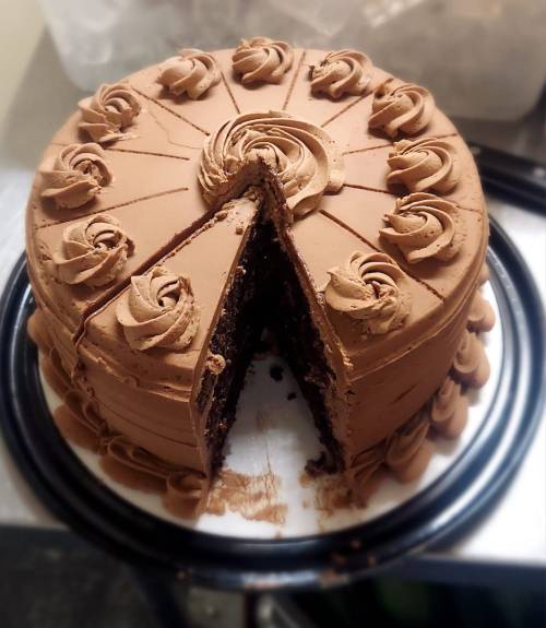 A chocolate cake with decorative frosting and a slice cut out, resting on a black plate.