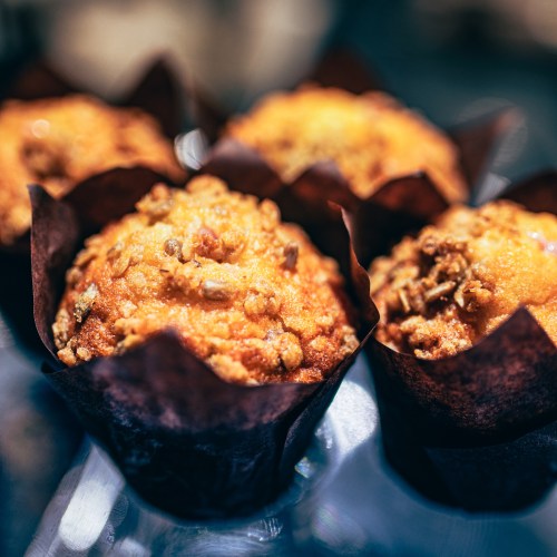 Close-up of freshly baked muffins with a crumbly topping, wrapped in dark paper liners.