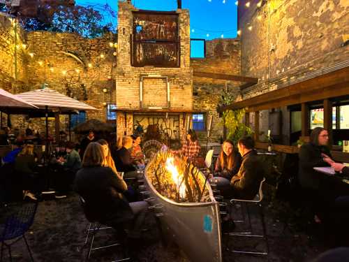 A cozy outdoor gathering around a fire in a rustic courtyard, with string lights and people enjoying the evening.