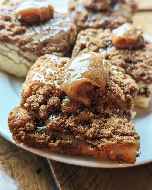 A close-up of cinnamon coffee cake topped with a dollop of caramel sauce on a white plate.