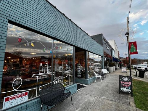 A storefront with large windows displaying colorful decorations, a sidewalk, and festive lights in the background.