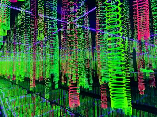 Colorful spirals in vibrant green and pink hang from a dark ceiling, creating a mesmerizing, abstract light display.