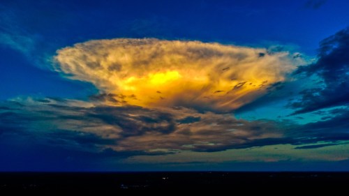 A dramatic cloud formation illuminated by sunset, with vibrant yellow and orange hues against a blue sky.
