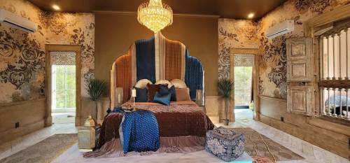 Luxurious bedroom featuring a chandelier, ornate wallpaper, a plush bed with decorative pillows, and elegant furnishings.