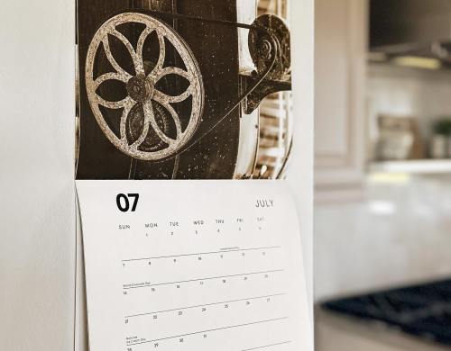A close-up of a calendar page for July, featuring a decorative wheel design in the background.