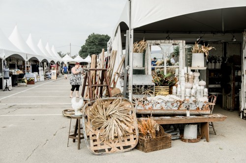 A bustling outdoor market with tents, showcasing vintage decor, plants, and handmade items.