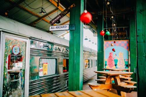 A colorful diner interior featuring a vintage train car, festive decorations, and wooden picnic tables.