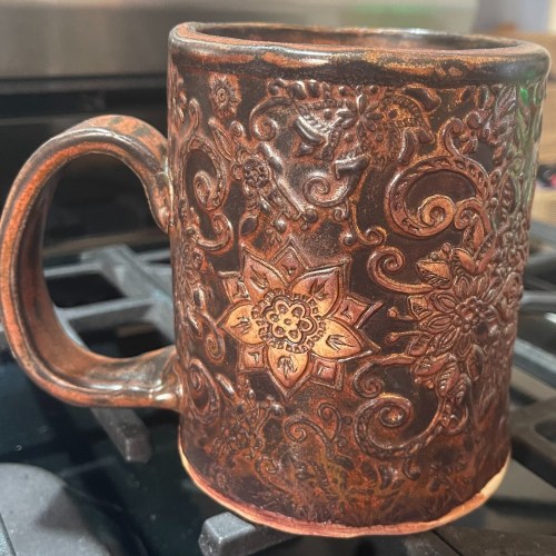 A decorative, embossed ceramic mug with floral patterns, resting on a stovetop.