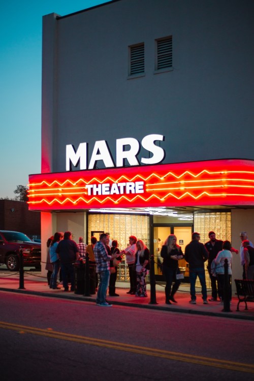A crowd gathers outside the Mars Theatre, featuring a bright red marquee at dusk.