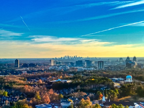 A panoramic view of a city skyline in the distance, surrounded by trees and buildings under a clear blue sky.