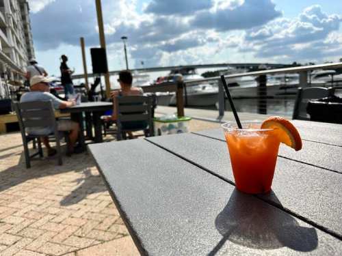 A refreshing cocktail sits on a table by the water, with people enjoying the view and live music in the background.