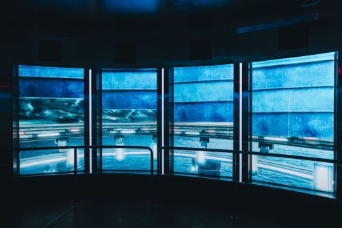 A dark room with four large screens displaying blue abstract visuals and illuminated by soft lights.