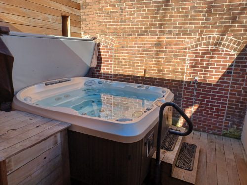 A hot tub on a wooden deck, surrounded by a brick wall, with sunlight casting shadows.