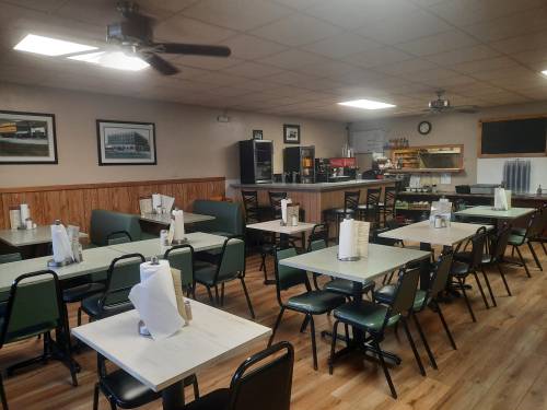 A cozy diner interior with green booths and tables, featuring a counter and a menu board in the background.