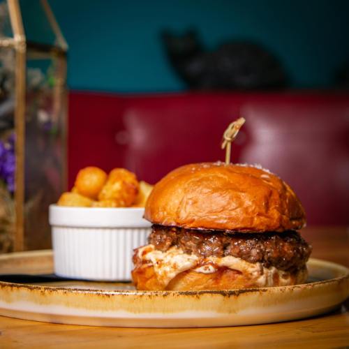 A juicy burger on a toasted bun, served with a side of golden-brown potato bites in a white dish.