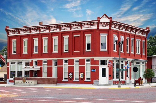 Historic red brick city hall building with large windows and decorative trim, set against a blue sky.