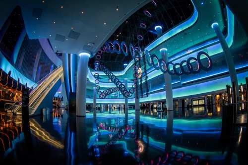 A modern, brightly lit interior with colorful lighting, abstract sculptures, and reflective floors.