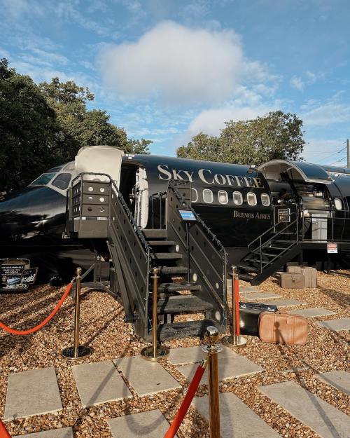 A black airplane converted into a coffee shop, with stairs leading up and a red carpet entrance.