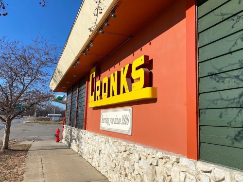 Sign for "Cronk's" restaurant, featuring bold yellow letters on a colorful exterior with a stone base.