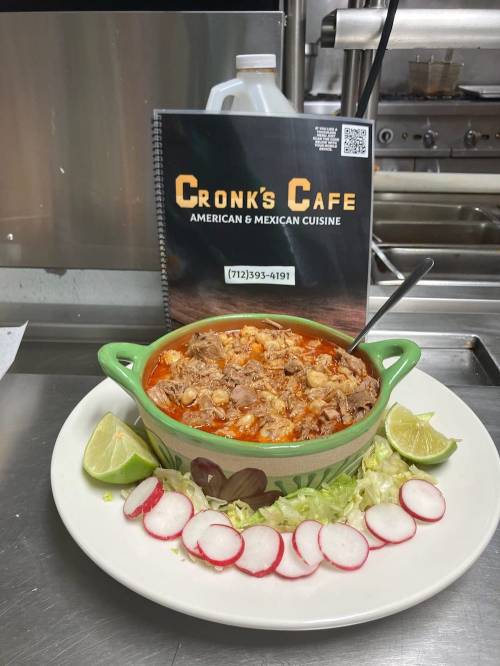 A bowl of hearty stew with meat, garnished with lime, lettuce, and radishes, next to a menu for Cronk's Cafe.