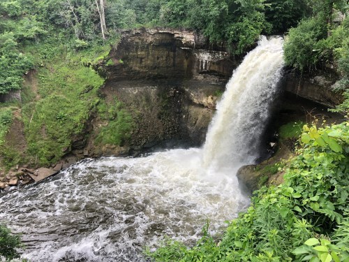 A waterfall cascades into a rocky pool, surrounded by lush greenery and trees.