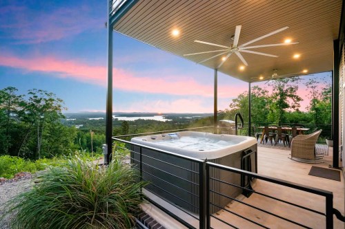 A hot tub on a deck with a scenic view of trees and a lake at sunset, featuring a dining area nearby.